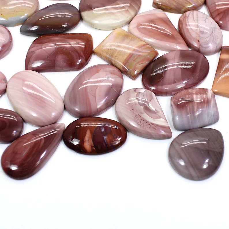 May include: A collection of polished, natural, red, pink, and white gemstone cabochons. The cabochons are various shapes and sizes, including oval, teardrop, and rectangular.