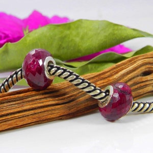 Può includere: Due perline di pietra preziosa rossa su un braccialetto a catena d'argento. Le perline sono sfaccettate e hanno un colore rosso intenso. La catena è di design a corda intrecciata.