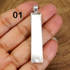 May include: Silver pendant with a rectangular blank space for adding a design or image. The pendant is approximately 2 inches long.