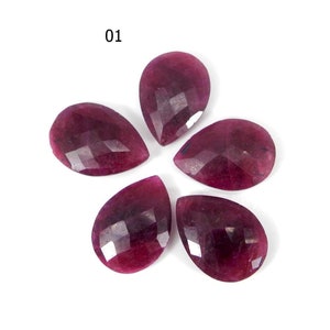 May include: Six faceted pear-shaped ruby red gemstones. The gemstones are arranged in a flower shape.