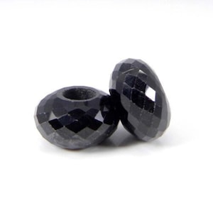 Peut inclure: Deux perles de pierres précieuses facettées noires avec un trou au centre. Les perles sont rondes et ont une finition brillante.