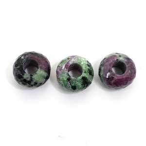 May include: Three green and purple gemstone beads with a hole in the centre. The beads are faceted and have a rough, natural look.
