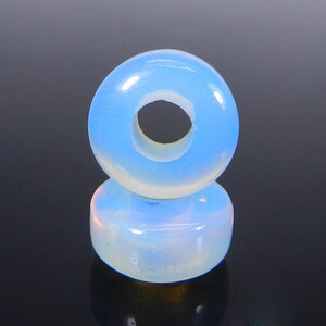 May include: A light blue opal bead with a hole in the center. The bead is round and has a smooth, polished surface.