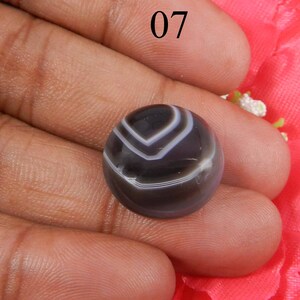 May include: A black and white banded agate cabochon with a striped pattern. The cabochon is round and has a smooth, polished surface.