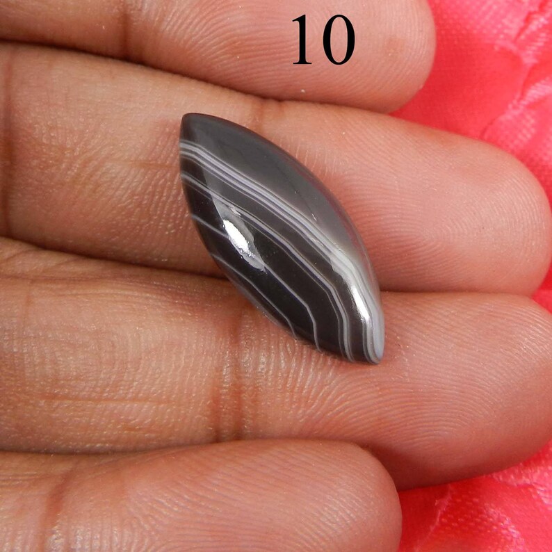 May include: Black and white banded agate cabochon with a pointed oval shape. The cabochon is approximately 1 inch long.