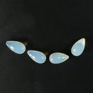 May include: Four teardrop-shaped opal gemstones in a light blue color. The gemstones are arranged in a semi-circle on a black background.