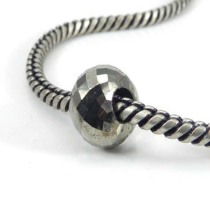 Peut inclure: Un bracelet à breloques argenté avec une perle de pyrite facetée. La perle est de couleur gris foncé et a un éclat métallique.