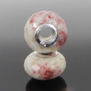 May include: Two white and red gemstone beads with a silver spacer between them. The beads are faceted and have a hole in the center. The silver spacer is stamped with "925".