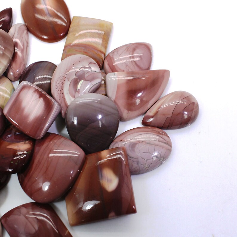 May include: A collection of polished, natural, red, brown, and white agate cabochons. The cabochons are various shapes and sizes, including oval, teardrop, and square.