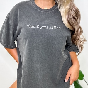 May include: A dark gray oversized t-shirt with the text "thank you aiMee" printed in white.