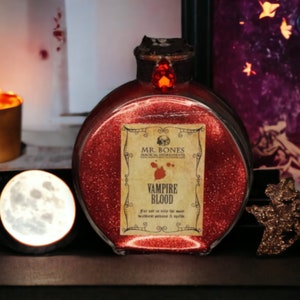 May include: A red glass bottle with a gold label that reads "Mr. Bones Magical Ingredients" and "Vampire Blood". The bottle is filled with red glitter and has a cork stopper.