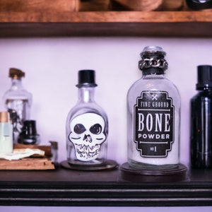 May include: A glass bottle with a skull sticker and a label that reads "Fine Ground Bone Powder No. 1" sits on a shelf with other bottles.