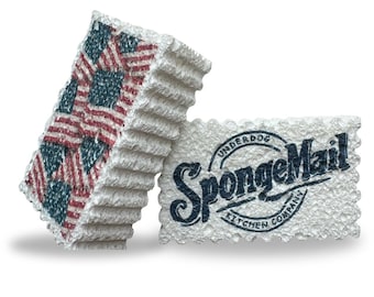 Könnte beinhalten: Zwei weiße Küchenschwämme. Ein Schwamm zeigt ein Muster aus amerikanischen Flaggen in Rot, Weiß und Blau. Der andere Schwamm trägt den Text "SpongeMail Kitchen Company" in Marineblau.