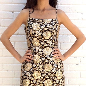 Peut inclure: Une robe sans manches noire et dorée à motif floral. La robe a un décolleté carré et une silhouette ajustée.