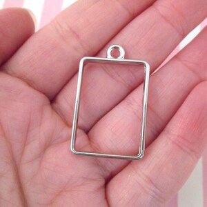 May include: Silver metal pendant frame with a rectangular shape and a loop at the top for hanging.