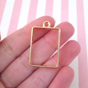 May include: Gold-toned metal pendant with a rectangular frame. The frame is open and ready to be filled with resin or other materials.