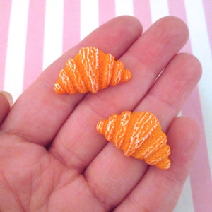 Puede incluir: Dos encantos de arcilla polimérica en forma de croissant de color naranja y blanco. Los encantos miden aproximadamente 2,5 cm de largo y son perfectos para agregar un toque de fantasía a tus joyas o manualidades.