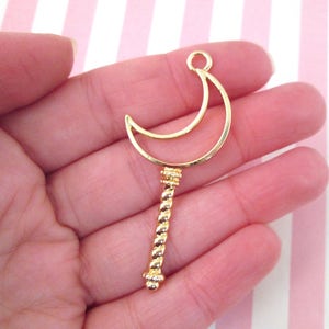 May include: Gold-toned metal charm featuring a crescent moon shape with a twisted stem. The charm is perfect for jewelry making or crafting projects.