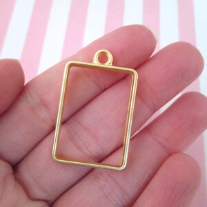 May include: Gold-toned metal pendant frame with a rectangular shape and a loop at the top for hanging.