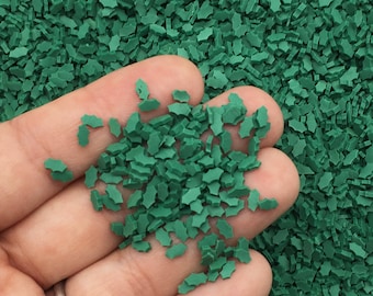 May include: Green holly leaf sprinkles for baking and decorating. The sprinkles are small and have a slightly irregular shape.