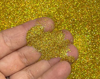 May include: A close-up of fine gold glitter with iridescent shimmer. The glitter is loose and has a fine texture.