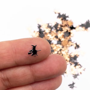 May include: Black witch silhouette on a broomstick, surrounded by a scattering of black and gold glitter.