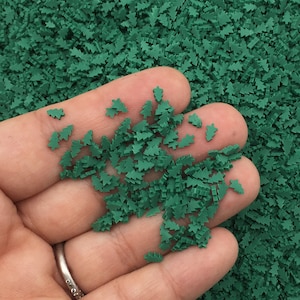 Pode incluir: Um punhado de granulado verde de árvore de Natal. Os granulados são pequenos e têm uma forma plana, bidimensional.