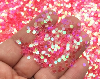 May include: Pink iridescent glitter with a hexagonal shape. The glitter is loose and scattered on a surface.
