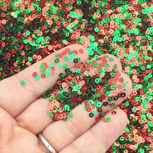 Op de afbeelding: Een handvol rode, groene en gouden iriserende pailletten. De pailletten zijn klein en rond en perfect voor knutselen of decoreren.