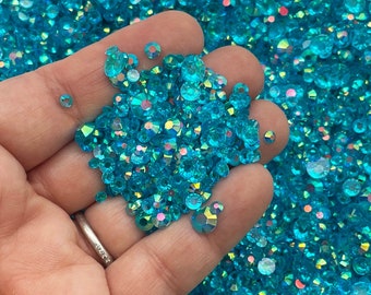 May include: A large quantity of turquoise blue iridescent rhinestones. The rhinestones are small and have a faceted, sparkly finish.
