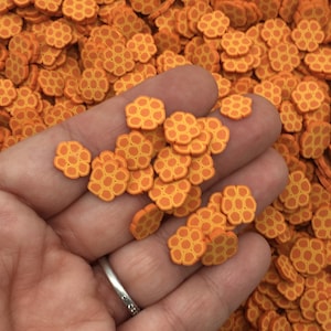 May include: Orange and yellow honeycomb-shaped sprinkles. The sprinkles are small and perfect for decorating cakes, cupcakes, and other desserts.