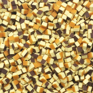 May include: A close-up image of a large pile of small, square-shaped candies. The candies are half yellow and half brown.