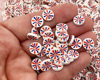 Op de afbeelding: Een hand die een stapel kleine, ronde witte keramische knopen vasthoudt met een rood en blauw swirl-ontwerp.