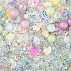 May include: A mix of iridescent clear, pink, and green glitter, seashells, and pearls.