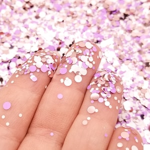 Op de afbeelding: Een hand bedekt met roze en zilveren glitterconfetti. De confetti is in verschillende maten en vormen.