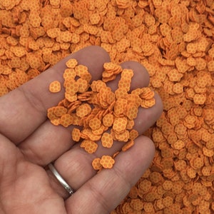 May include: Orange and yellow honeycomb-patterned sprinkles in a hand. The sprinkles are small and round, and they are perfect for decorating cakes, cupcakes, and other desserts.