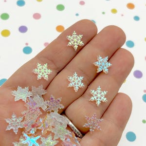 May include: A handful of iridescent white snowflake-shaped embellishments. The snowflakes are made of plastic and have a holographic finish.