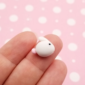 May include: A small white bunny charm with pink ears. The charm is made of polymer clay and is perfect for adding a touch of whimsy to your crafts.