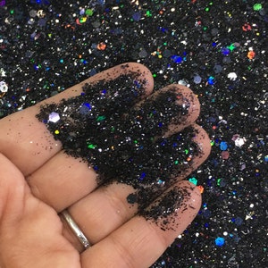 May include: A hand holding a pile of black glitter with iridescent rainbow flecks.