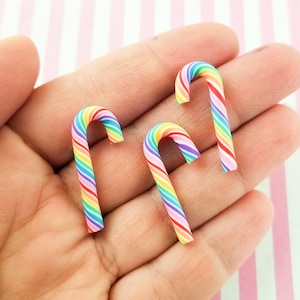 May include: Three rainbow candy cane charms made of polymer clay. The candy canes are red, orange, yellow, green, blue, and purple.