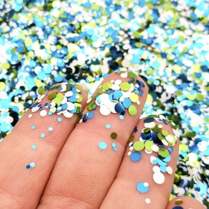May include: A close-up of a hand holding a variety of colorful glitter. The glitter is a mix of blue, green, and white, and it is arranged in a random pattern. The glitter is perfect for crafting and decorating.