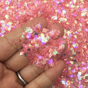 May include: A close-up of pink iridescent glitter with a variety of sizes and shapes. The glitter is being held in a hand.