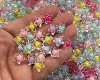 May include: A close-up of a hand holding a pile of colorful star-shaped beads. The beads are made of clear plastic with a variety of pastel colors, including pink, blue, yellow, and green.