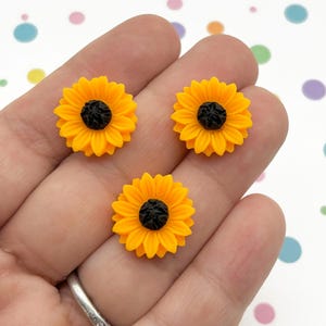 May include: Three yellow sunflower-shaped resin embellishments with black centers. The embellishments are small and perfect for adding a touch of whimsy to crafts.