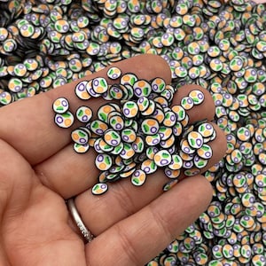 Könnte beinhalten: Ein großer Haufen kleiner, runder, bunter Harzembellen. Jede Embellishment hat einen schwarzen Umriss und eine weiße Mitte mit einem grünen, orangefarbenen und violetten Design.