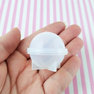 May include: A clear plastic mold for making round resin crafts. The mold has a smooth, rounded surface and a flat base.
