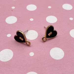 Puede incluir: Un par de pendientes de corazón de oro con acabado de esmalte negro. Cada corazón tiene un diseño de ojo de cerradura en el centro.