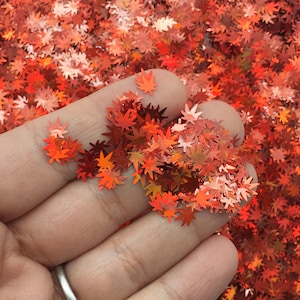 May include: A handful of orange and red glitter maple leaves. The leaves are iridescent and have a holographic finish.