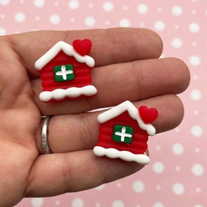May include: Two red and white Christmas houses with a green door and a white plus sign on the door. Each house has a small red heart on top.