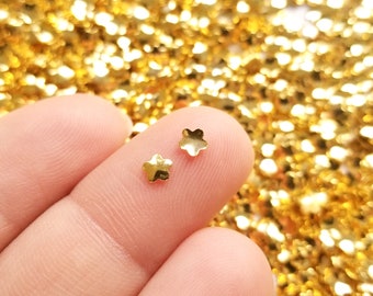May include: Two gold star-shaped embellishments on a fingertip, against a background of gold glitter.